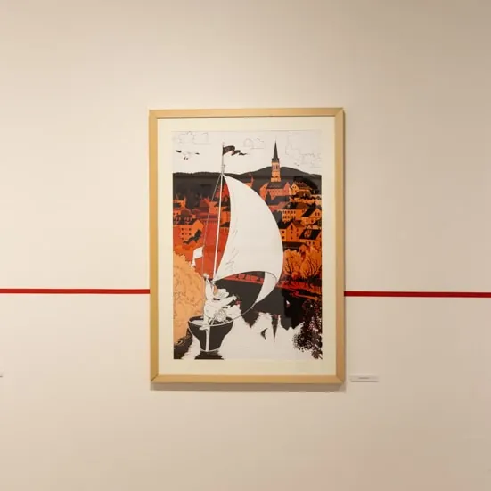 Uokvirjena stripovska ilustracija z jadrnico na belem zidu galerije