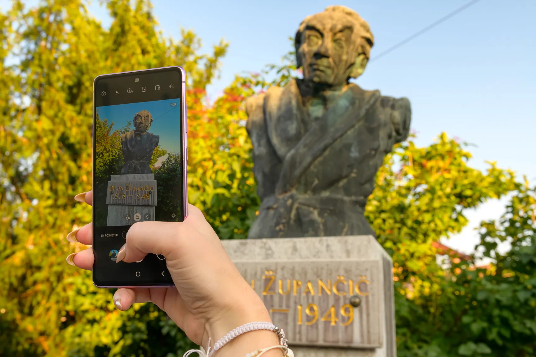 Obiskovalka s telefonom fotografira kip Otona Župančiča v Vinici